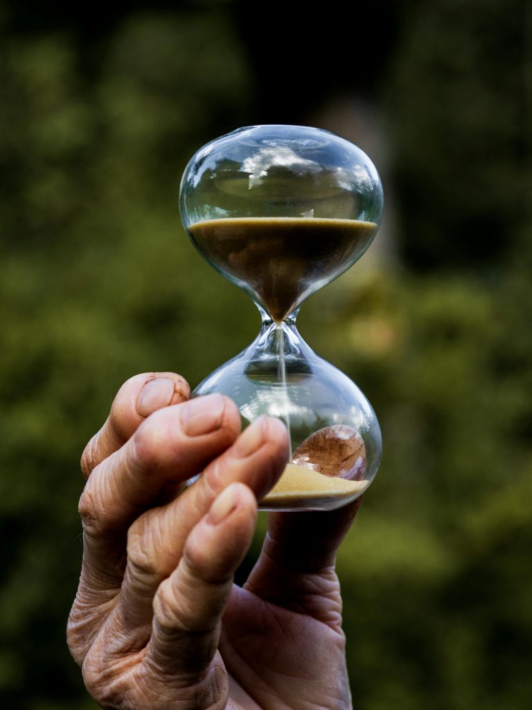 Hand holding an hourglass against a natural backdrop, symbolizing epigenetic clocks and the velocity of biological aging